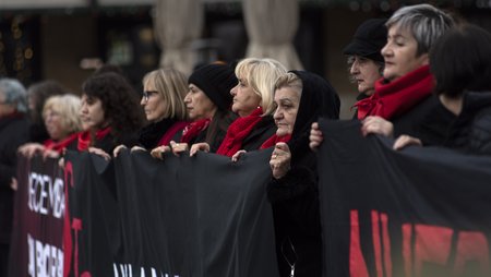 Numerous women dressed in black and red are seen at a demonstration. They are standing in a row holding a demonstration banner. The inscription is not visible. 