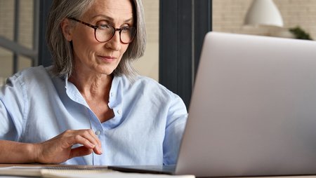 Eine ältere Frau sitzt vor einem Laptop und nimmt an einem Webinar teil.