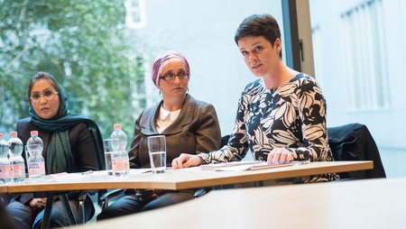 Humaira Rasuli, Sabiha Husic and Jeannette Böhme sitting at a conference table in a room in the German Federal Parliament building.