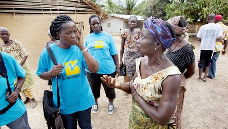  Einige Mitarbeiterinnen des Teams von Medica Liberia diskutieren in einer liberianischen Dorfgemeinde miteinander. Sie tragen blaue T-Shirts mit dem Aufdruck „medica mondiale“. 