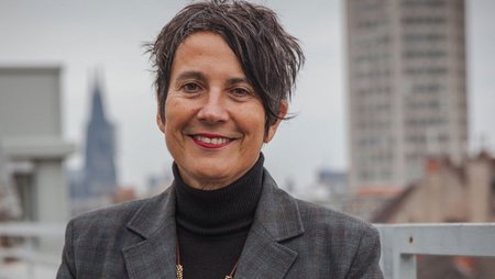 Eine Frau mit grauem Blazer steht auf einer Dachterrasse mit Kölner Dom im Hintergrund. Es ist Monika Hauser, Vorstandsvorsitzende bei medica mondiale.