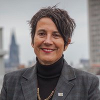 Eine Frau mit grauem Blazer steht auf einer Dachterrasse mit Kölner Dom im Hintergrund. Es ist Monika Hauser, Vorstandsvorsitzende bei medica mondiale.