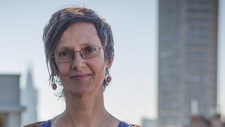 Eine Frau in einer Brille und braunem Oberteil steht auf einer Dachterrasse mit Kölner Dom im Hintergrund. Es ist Pia Frohwein, Fachreferentin für Traumaarbeit bei medica mondiale.