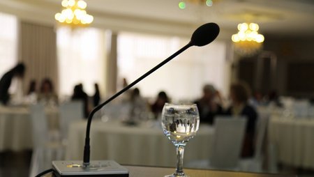 Mikrofon und ein Glas Wasser auf einem Redner:innenpult.