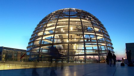 An evening photo of the glass dome of the German Federal Parliament building with interior lighting. 